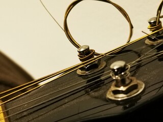 Tuning peg on acoustic guitar headstock with strings. Close up photo