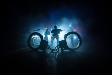 Police raid at night and you are under arrest concept. Silhouette of handcuffs with police car on backside. Image with the flashing red and blue police lights at foggy background.