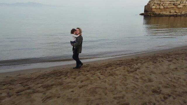 Happy mother walks with her little daughter on the beach with the sea and waves in the background. Take air.