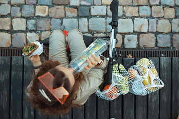 stylish woman in overall eating while sitting outside in city