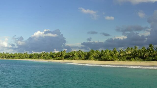 Wild sandy beach with palm jungle. Blue sea water and blue cloudy sky near the peninsula. Bright tropical landscape.
