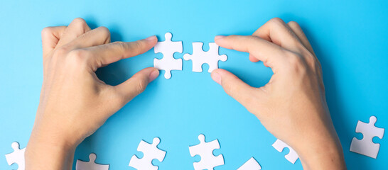 hands connecting couple white puzzle jigsaw pieces on blue background. Concept of solutions, mission, success, goals, cooperation, partnership, strategy and puzzle day