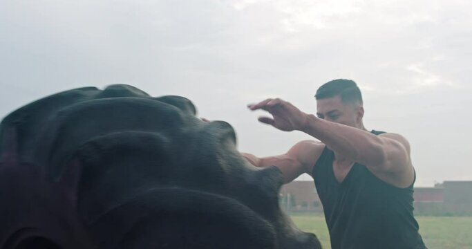 Athletic man flips over tire in a foggy field
