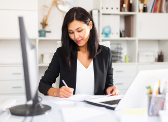 Young asian woman working and signs documents at the office table