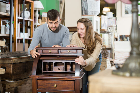 Loving couple satisfied with purchase of old stylish writing cabinet at home
