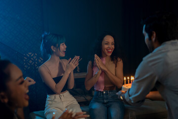 Portrait of cheerful woman laughing and clapping while man presenting cake with candles at midnight during house party for christmas and birthday