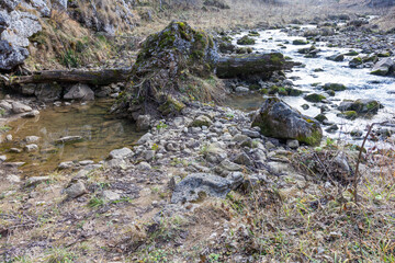 Naklejka na ściany i meble autumn morning, walking along the bed of a mountain river that has become shallow by the beginning of the winter period and exposing its rocky bottom.