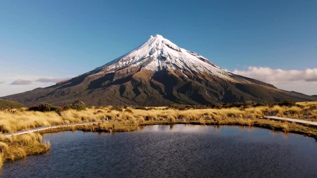 Tourists waiting for reflection of Taranaki volcano at Pouakai Tarn -  flyover drone shot. Famous hiking area in New Zealand.