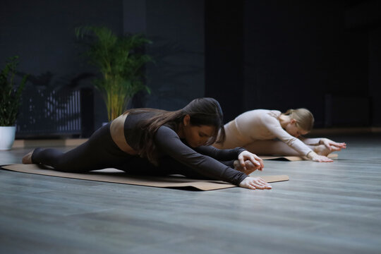 Two sportive women practicing doing split together in stretching studio. Group training, teamwork concept