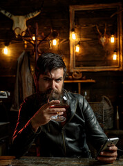 Fototapeta na wymiar Stylish elegant bearded man holds whiskey glass. Social media addiction, alcohol abuse.