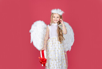Playful angelic little girl. Little blonde angel with white wings holds gift. Cute angel child girl...