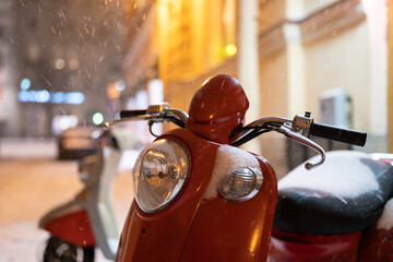 Red retro vintage motor scooter under falling snow at night, selective focus. Electric motorcycle...
