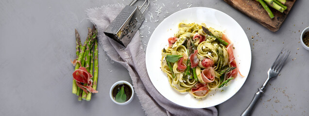 Pasta with asparagus and prosciutto on gray background.