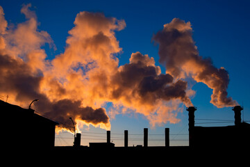 Factory chimneys smoke toxic substances above industrial building silhouette over beautiful sunset or sunrise blue sky