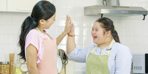 Asian young happy chubby down syndrome autistic daughter in apron and lovely mother standing...
