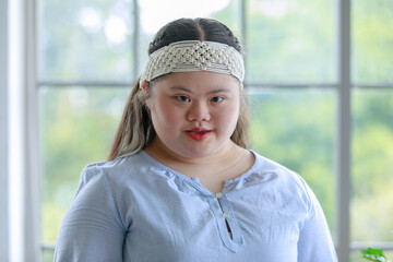 Portrait close up shot of Asian young happy chubby down syndrome autistic autism girl model wearing white knitted headband standing smiling look at camera in front blurred glass windows background