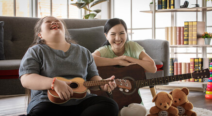 Asian lovely mother holding guitar sit smiling on sofa couch in living room at home teaching young...