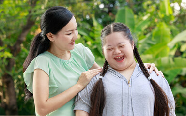 Portrait shot of Asian mother and young chubby down syndrome autistic autism little cute girl with braid pigtail hairstyle stand hugging cuddling embracing together with love smiling look at camera