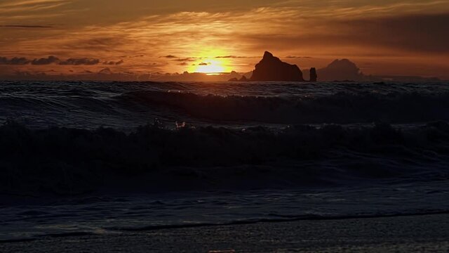 Incredible stunning slow motion tilting up shot of a beautiful golden orange sunset at the famous Ruby Beach near Forks, Washington during golden hour on a warm summer day with small rocks and waves.
