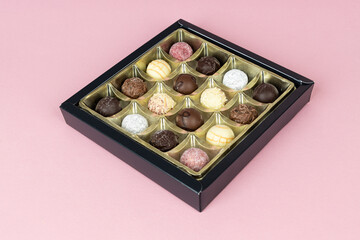 Box of various chocolate candies on pink background