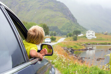 Cute child, peeping out of a window car, looking at a beautiful landcape view in Lofoten