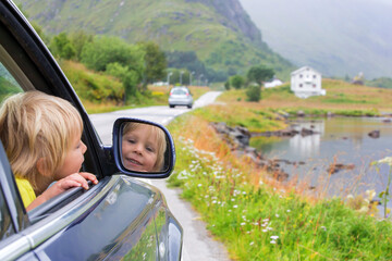 Cute child, peeping out of a window car, looking at a beautiful landcape view in Lofoten