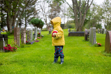 Sad little child, blond boy, standing in the rain on cemetery, sad person, mourning