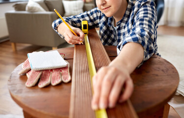 Obraz premium repair, diy and home improvement concept - close up of happy smiling woman with ruler and pencil measuring wooden board at home