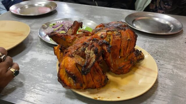 Cinematic video of Famous Indian dish i.e. full tandoori chicken. A fired chicken leg with spices in it.Fried on black colored large fryer. Served in the iftar also