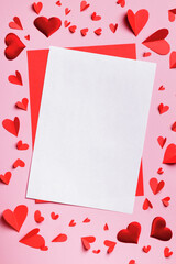 Love letter valentine day concept. Mock up of a blank white sheet of paper and paper hearts on a pink background.