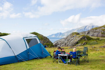 Happy family with three kids, wild camping in Norway summertime, people having breakfast adn coffee...