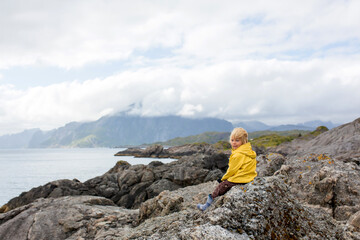 Fototapeta premium Child, enjoying a picturesque view from the edge of a cliff in Lofoten, Norway. Amazing beautiful norwegian nature