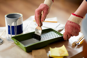 furniture renovation, diy and home improvement concept - close up of hands in gloves dipping brush in grey paint