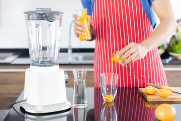 Closeup of healthye man with casual clothes is smiling and preparing orange juice to diet, in kitchen at home in holiday.