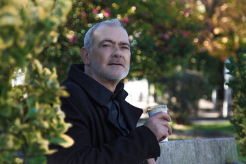 man in coat sitting relaxed on the park bench having coffee