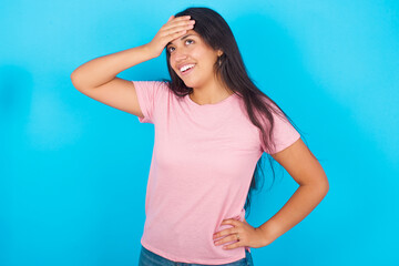 Young hispanic girl wearing pink T-shirt over blue background touching forehead, hears something surprising, glad receive good news, feels relieved. Almost got in trouble.