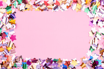 Bright colorful star-shaped confetti sparkles on a pink background, copy space.