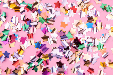 Bright colorful star-shaped confetti sparkles on a pink background.