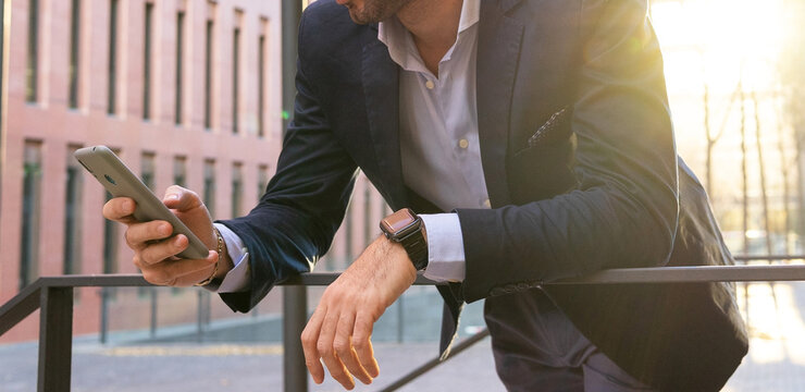 Unrecognizable businessman browsing smartphone while leaning on railing