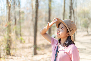 Happy beautiful young adventurous woman is smiling, using hand for covering face by hand to block, protect the sun in dry forest while walking and hiking to epic mountain. Outdoor adventure concept.