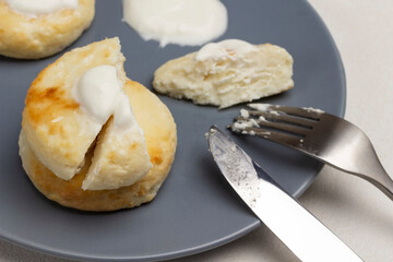 Cheesecakes with sour cream, fork and knife on gray plate.