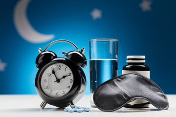 sleep disorder, bedtime and medicine concept - close up of alarm clock, eye mask, glass of water...
