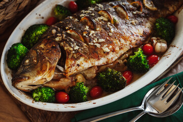 Baked fish carp with apples, broccoli, cherry tomatoes, garlic, lemon and herb spices in baking pan. Healthy eating concept.