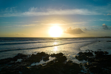 Sunset at the beach. Small rocks in front of water edge as silhouette. Cloudy sky.
