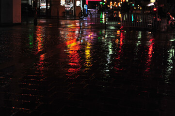 Colorful neon light reflections on cobblestone street scene in Paris.  Dark and rainy evening in...