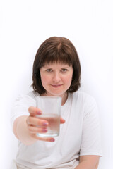 Young dark-haired caucasian smiling woman in white clothes hands you glass of water. Portrait on white background. Vertical frame