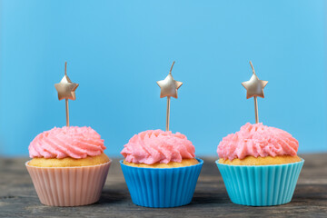 Bright holiday card with three cupcakes and candles in the form of stars on blue background. Muffin with pink buttercream frosting.