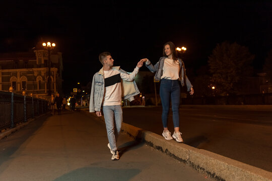 Young couple walks through the evening city. Guy holds the girls hand