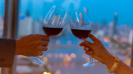 Selective focus of couple  hand with wine glasses have a romantic dinner on the rooftop with city as bokeh background