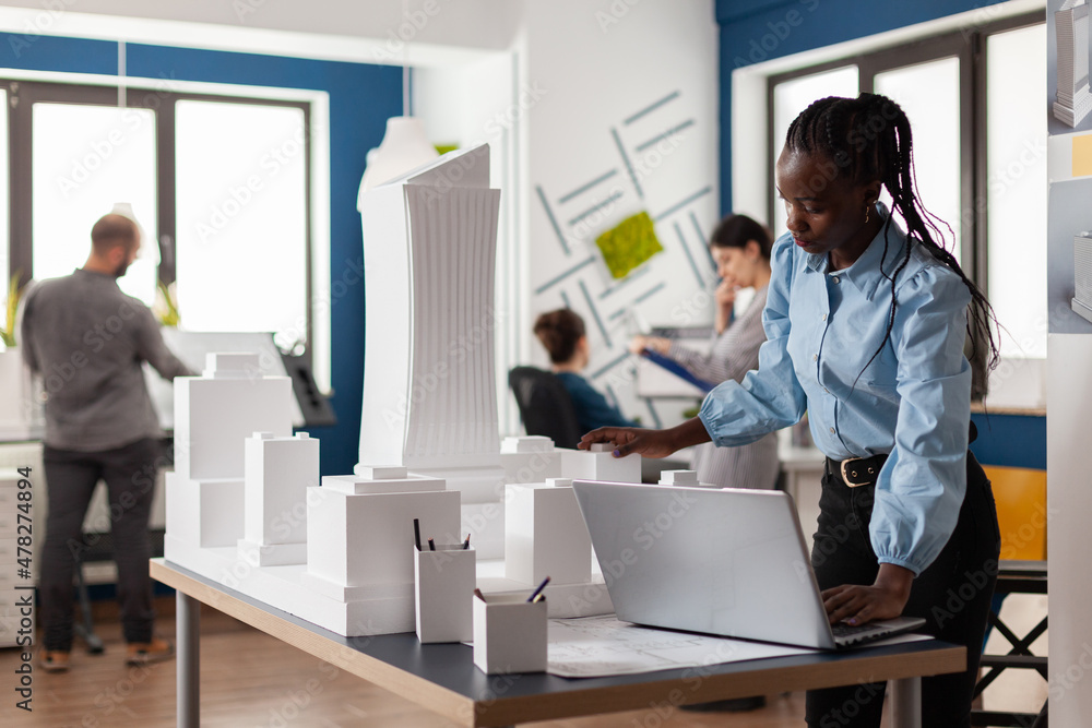 Poster standing architect with laptop looking at scale foam model of building from residential project. arc